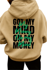 Beige hoodie with text on the back worn by a person, on a wooden floor background.