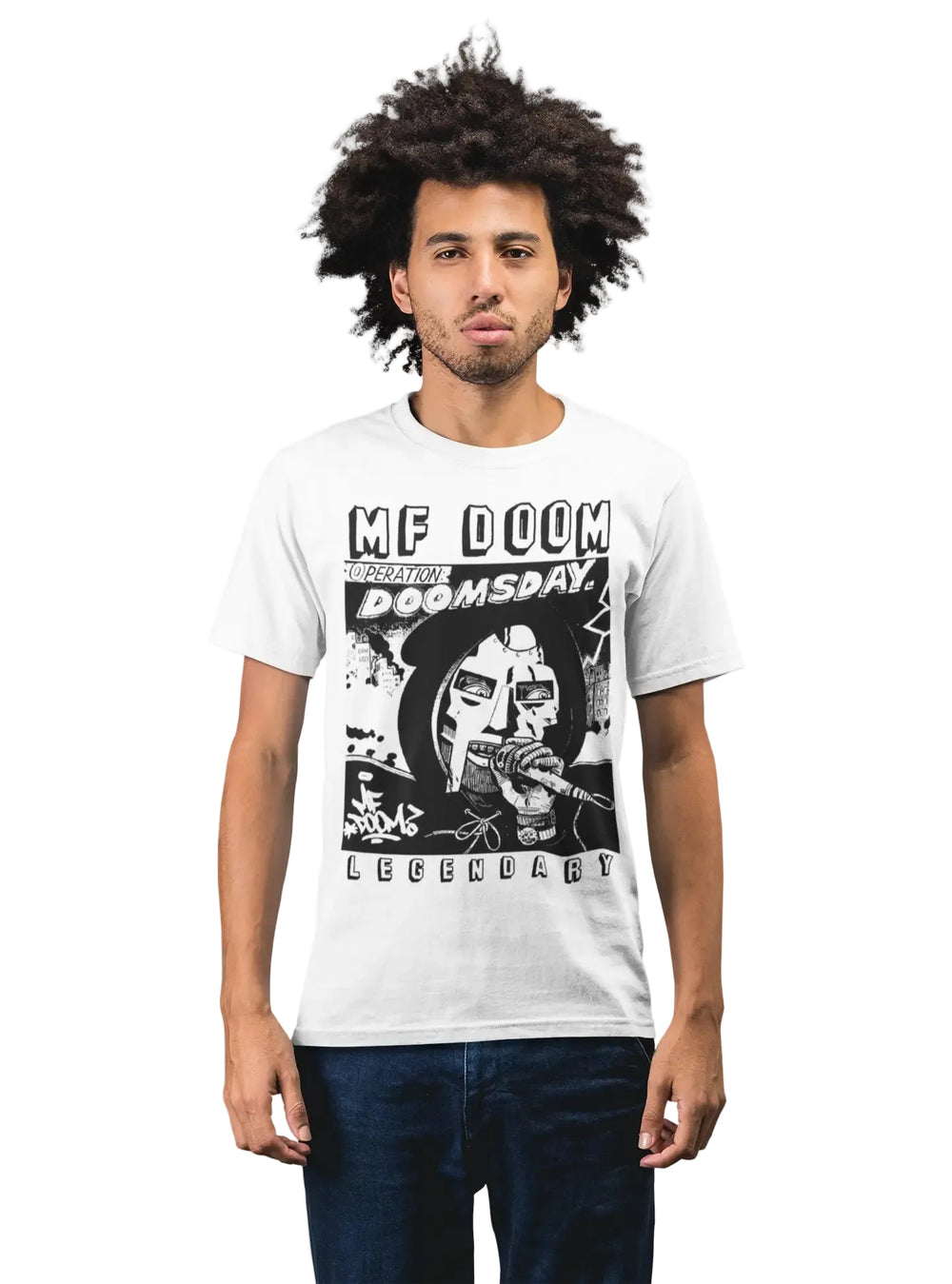 A man with an afro hairstyle wearing a white graphic t-shirt featuring a black and white print of MF Doom and the text 'MF DOOM REIGNITE DOOMSDAY LEGENDARY', paired with dark blue jeans, against a plain white background.