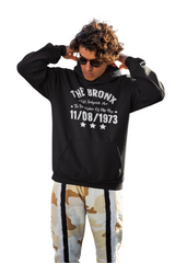 A person wearing a black hoodie with 'THE BRONX' and additional text on it, raising their fist in the air.