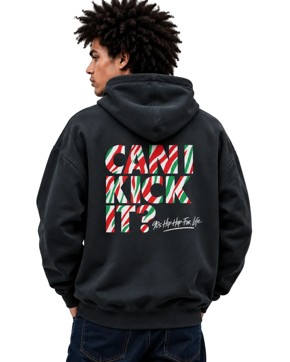 A man wearing a black hoodie from the back, featuring a large graphic on the back with the text 'CAN I KICK IT?' in red, green, and white striped candy cane shapes, and 'As Hip As Your Life' in white script below it.